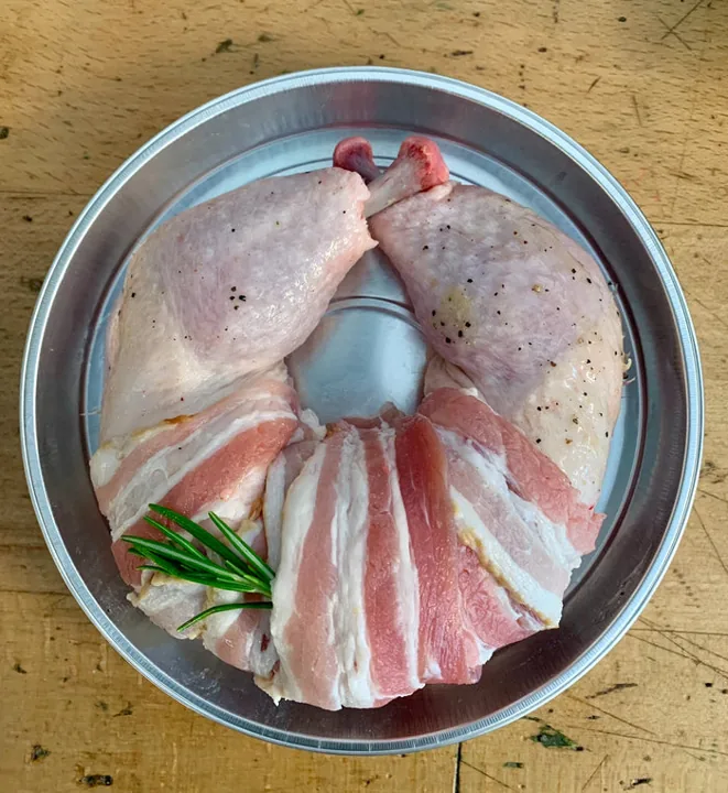 Raw chicken legs wrapped with bacon on a metal tray