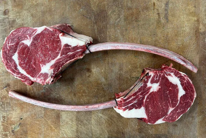 Two raw lamb chops with long rib bones on a wooden board