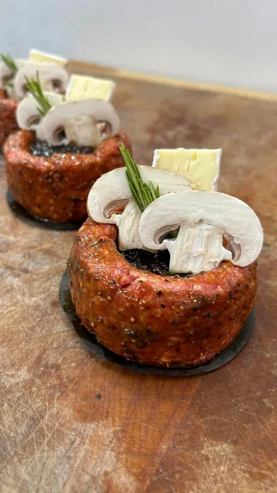 Prepared meat portions topped with mushrooms, cheese and herbs